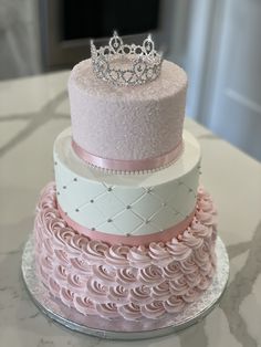 a three tiered cake with pink frosting and a tiara on top