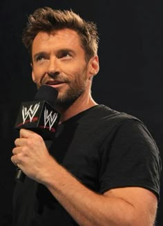 a man holding a microphone in his right hand and wearing a black shirt with the word wwe on it