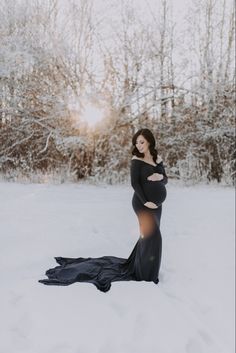 a pregnant woman standing in the snow wearing a black gown and holding her belly up