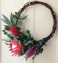 a wreath with flowers and greenery hanging on a door