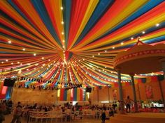 the ceiling is decorated with multicolored ribbons and string lights for an indoor event