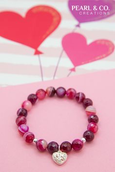 a bracelet with a heart charm is shown on a pink background and balloons are in the air