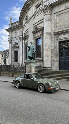 a green sports car parked in front of a building with a statue on the corner