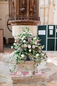 a vase with flowers and greenery is on the ground in front of a statue