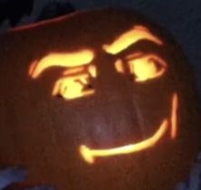 a carved pumpkin with the face of a man's head lit up at night