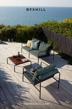 An outdoor lounge chair and outdoor lounge 2-seater sofa with dark green cushions and black frames and wooden top outdoor lounge table set on a wooden deck patio Lounge Sofa, Lounge Chair Outdoor