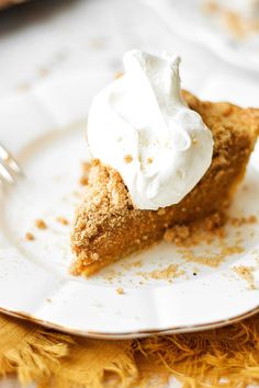 a piece of pie with whipped cream on top sits on a plate next to a fork