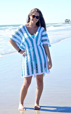 a woman standing on top of a beach next to the ocean wearing a blue and white striped dress