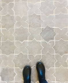 a person wearing black shoes standing in front of a tile floor with white and gray tiles