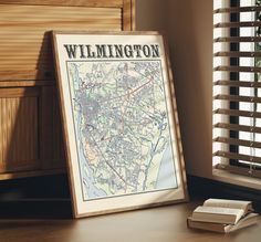 a framed map sitting on top of a wooden table next to a book and window