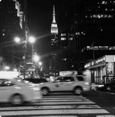 black and white photograph of cars driving down the street at night in new york city