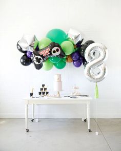 a table topped with balloons and an 8 number balloon wall mounted to the wall above it