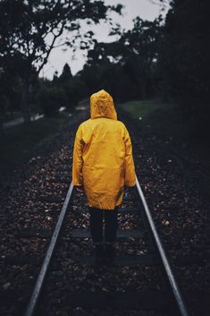 a person wearing a yellow rain coat walking on train tracks