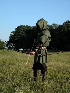 a man dressed in medieval clothing holding a bow and arrow while standing in a field