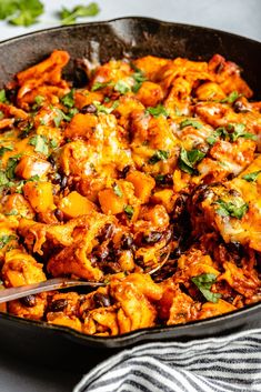 a skillet filled with chicken and cheese covered in cilantro sauce, garnished with parsley