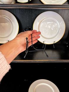 a person is holding some white plates in front of black racks with gold rims