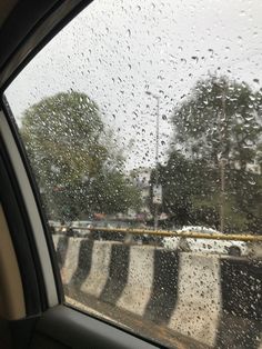 rain drops on the windshield of a car as it drives down a road in front of trees