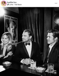 two men in tuxedos are sitting at a bar with drinks and snacks on the table