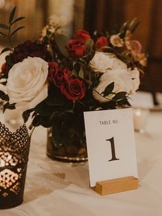 the table numbers are placed on small vases with flowers in them, along with candles and place cards