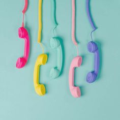 four different colored telephones hanging on a blue wall, one is pink, the other is green