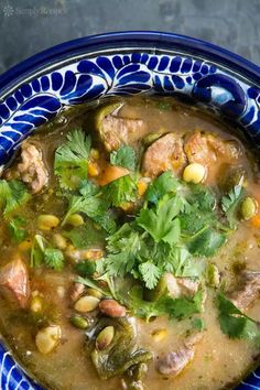 a blue and white bowl filled with meat, beans and cilantroo garnish