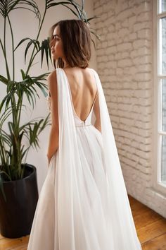 the back of a woman wearing a white wedding dress with a long veil over her shoulders