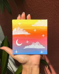 a hand holding up a small card with the sky and stars painted on it