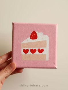 a hand holding up a small pink box with a cake on it