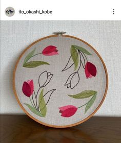 an embroidery project with red flowers and green leaves on white fabric in a wooden hoop