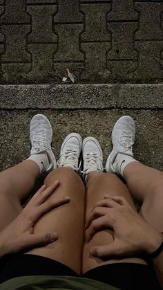 two people with their legs crossed sitting on the ground next to each other, both wearing white sneakers