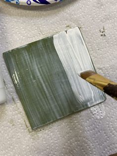 a painting brush is being used to paint a square piece of green and white paper