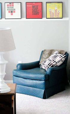 a blue chair sitting in front of a lamp next to a wall with pictures on it