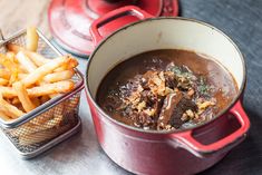 a red pot filled with food next to a container of french fries on top of a table