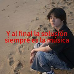 a young man sitting on top of a sandy beach next to footprints in the sand