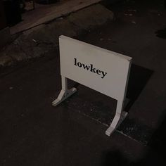 a white sign sitting on the side of a road next to a street light at night