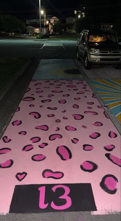 a pink and black street sign sitting on the side of a road next to a parked car