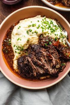 two bowls filled with meat, mashed potatoes and gravy on top of a wooden table