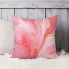 a pink and gold pillow sitting on top of a white fur covered bed next to a wooden headboard