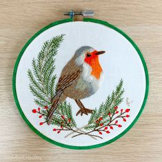 a small embroidered bird sitting on top of a green and white hoop with red berries