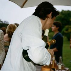 a man in a white robe is holding a wine bottle and looking down at the table