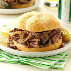 a pulled pork sandwich on a plate with potato wedges next to it and a can of beer in the background