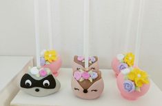 three cake pops decorated like animals with flowers on them, sitting on a white table