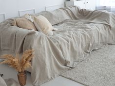 a living room with a couch covered in linens and pillows next to a potted plant