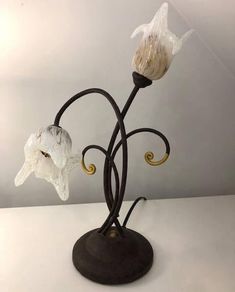 two white flowers sitting on top of a black metal stand next to a light bulb