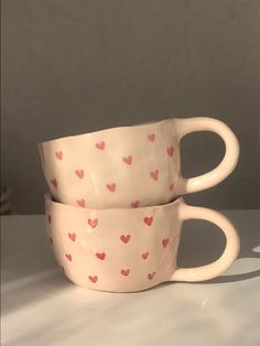 two coffee cups with hearts painted on them sitting side by side in front of a wall