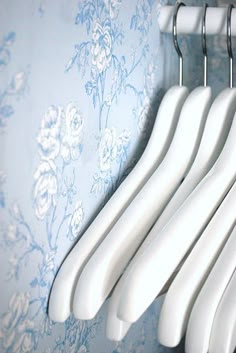 five white toothbrushes hanging from hooks on a blue floral wallpapered wall