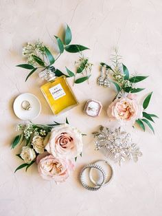 flowers and jewelry laid out on a white surface with a candle, ring, necklace, and perfume bottle