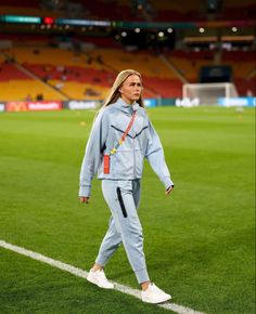 a woman walking across a soccer field in blue tracksuits and white sneakers with her hand on her hip