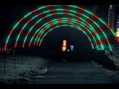 an archway with christmas lights on it in the snow at night and people walking down the path