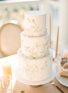 a white wedding cake sitting on top of a table next to wine glasses and plates